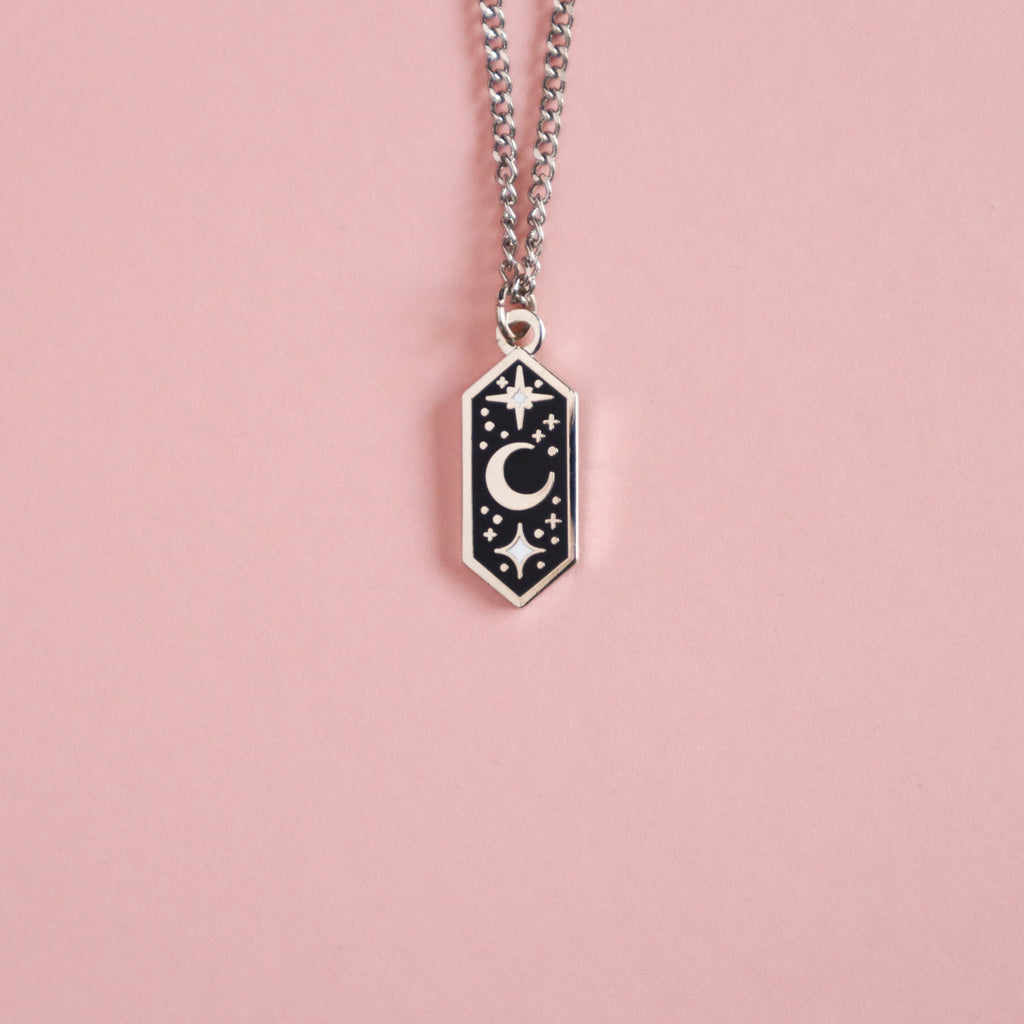 A silver Crescent Moon necklace. It's shaped like an elongated hexagon and feature a central crescent moon with stars above and below.