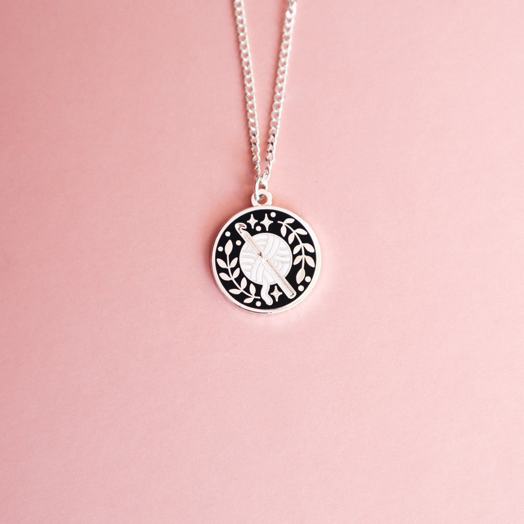 A silver crochet necklace on a pink background.