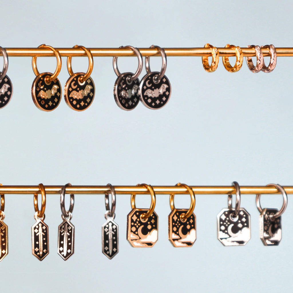 A selection of hanging Papio Press earrings. It features Bat, Dagger, Starry Sky and Star Huggie Hoops in both gold and silver.