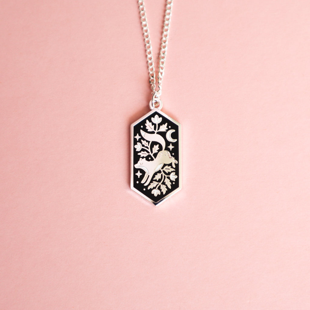 A silver floral fox necklace on a pink background.
