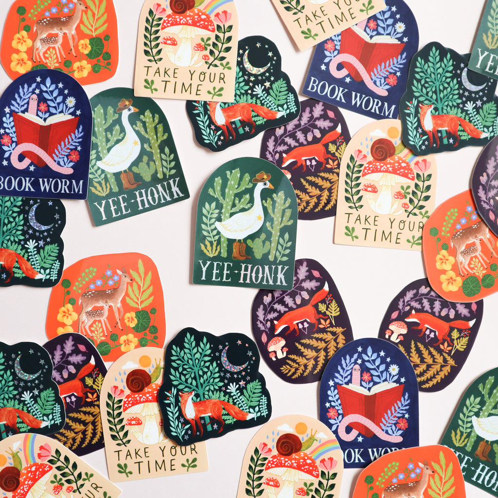 A photograph of a selection of stickers. Featured on the stickers are foxes, geese, books and florals. 