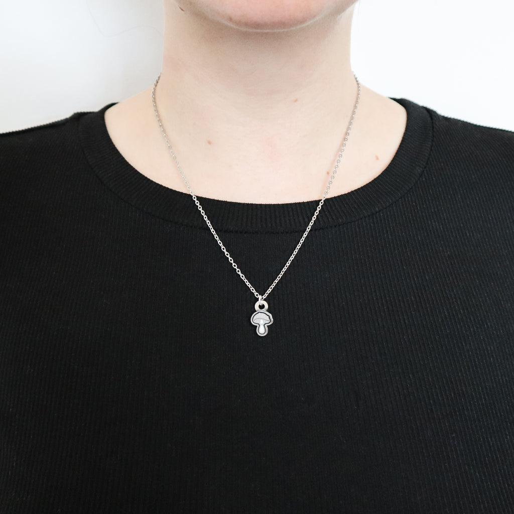 A silver mushroom necklace being worn by a model wearing a black top.