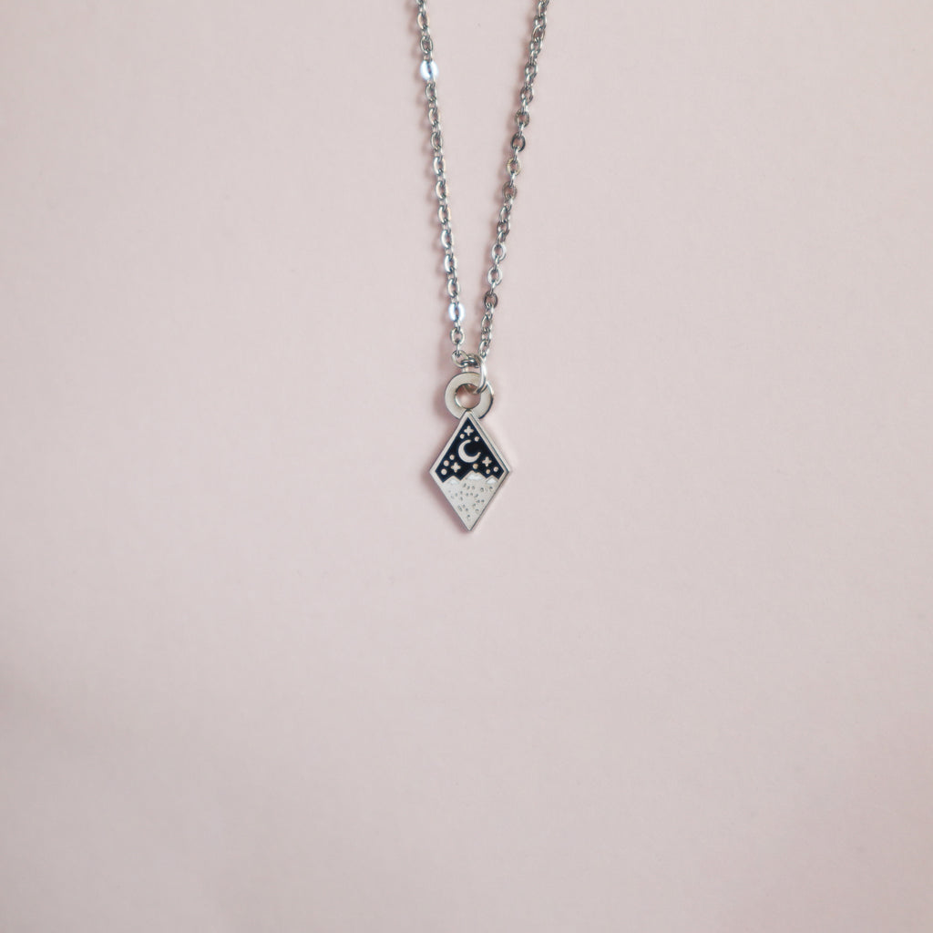 A silver mini moth necklace on a blush pink background.