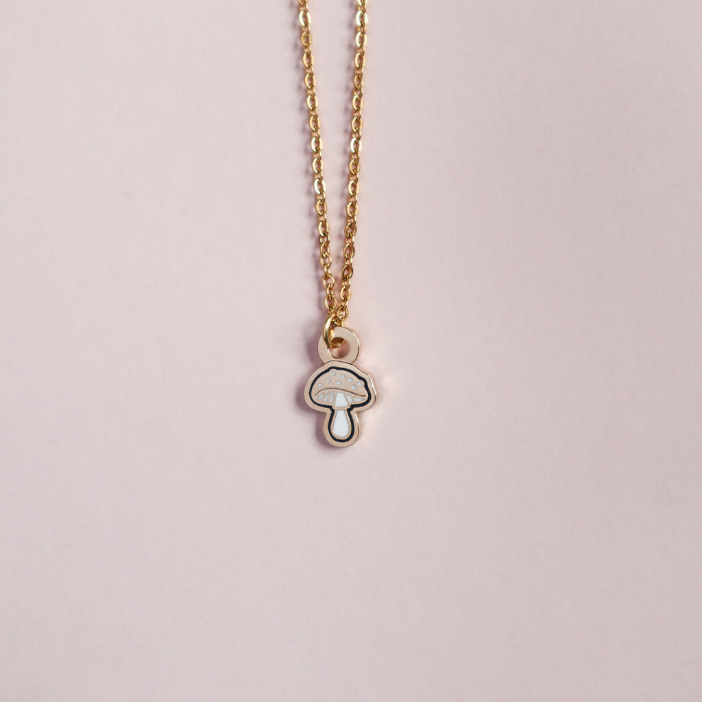 A gold mushroom necklace on a blush pink background.