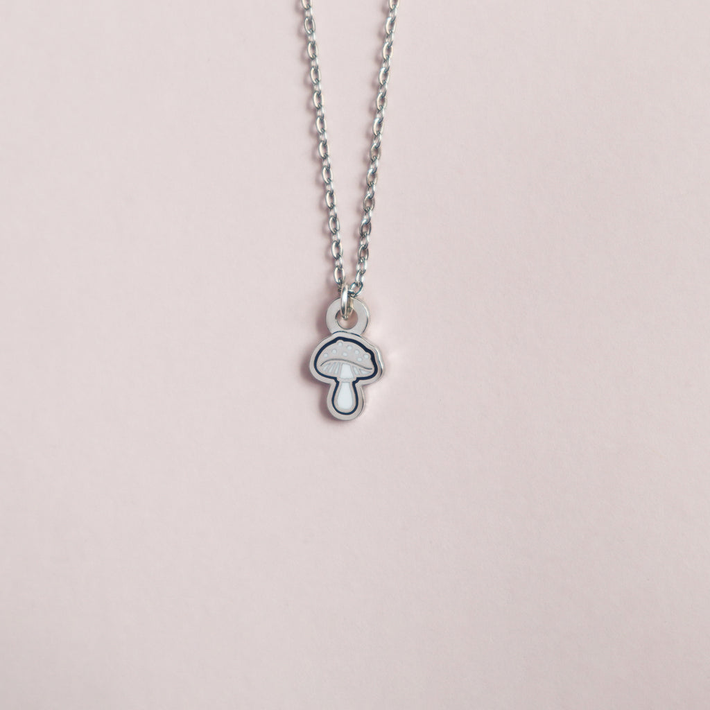 A silver mini mushroom necklace on a blush pink background.