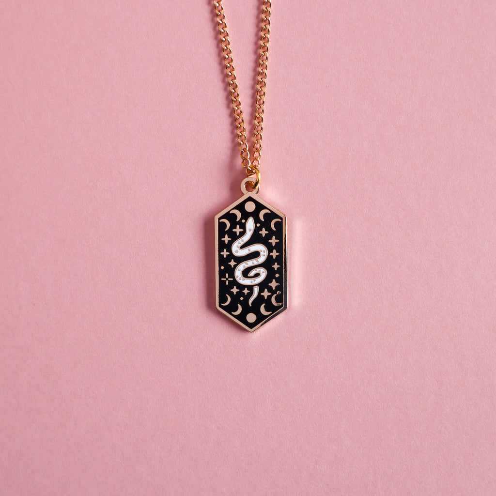 A gold snake necklace on a pink background.