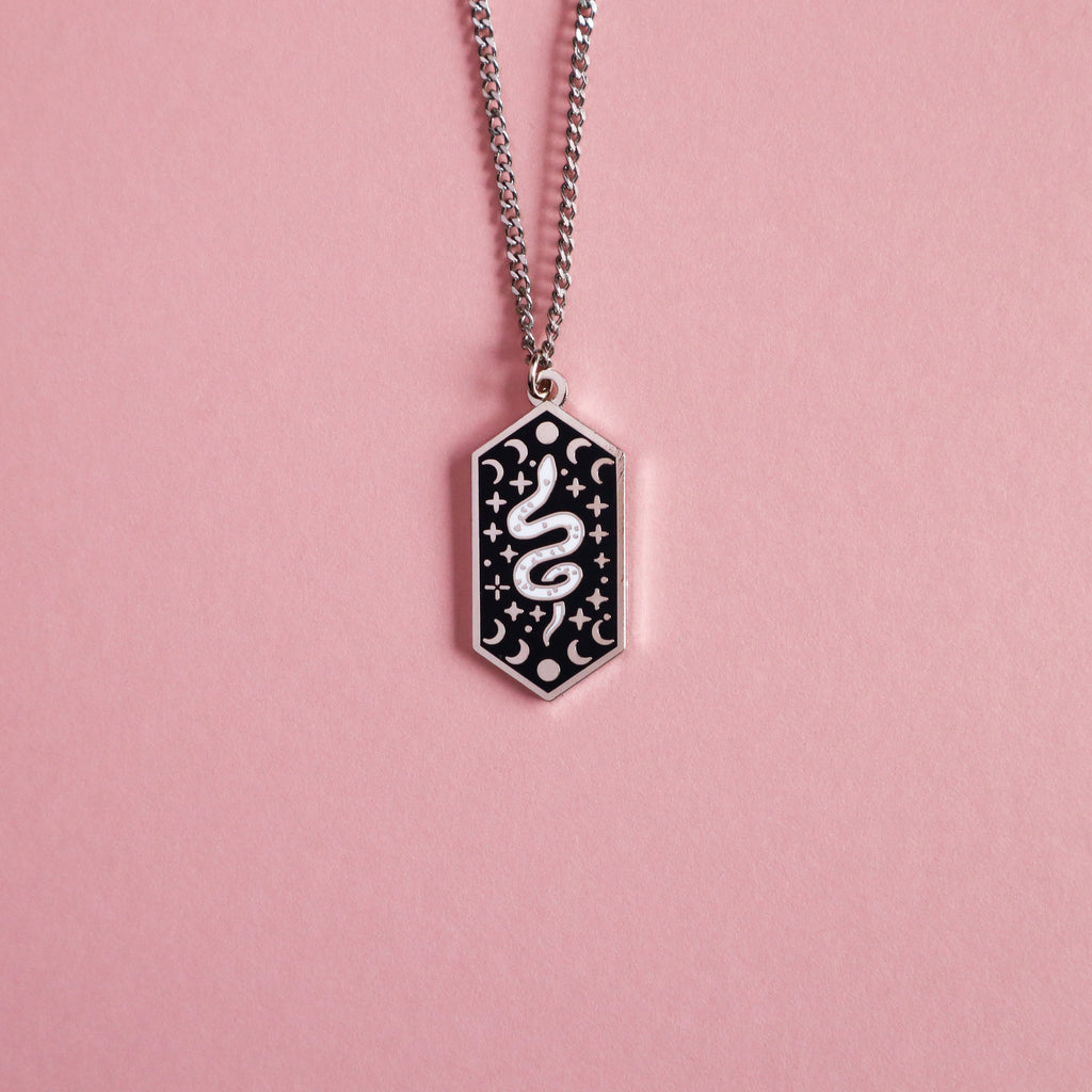 A silver snake necklace on a pink background.